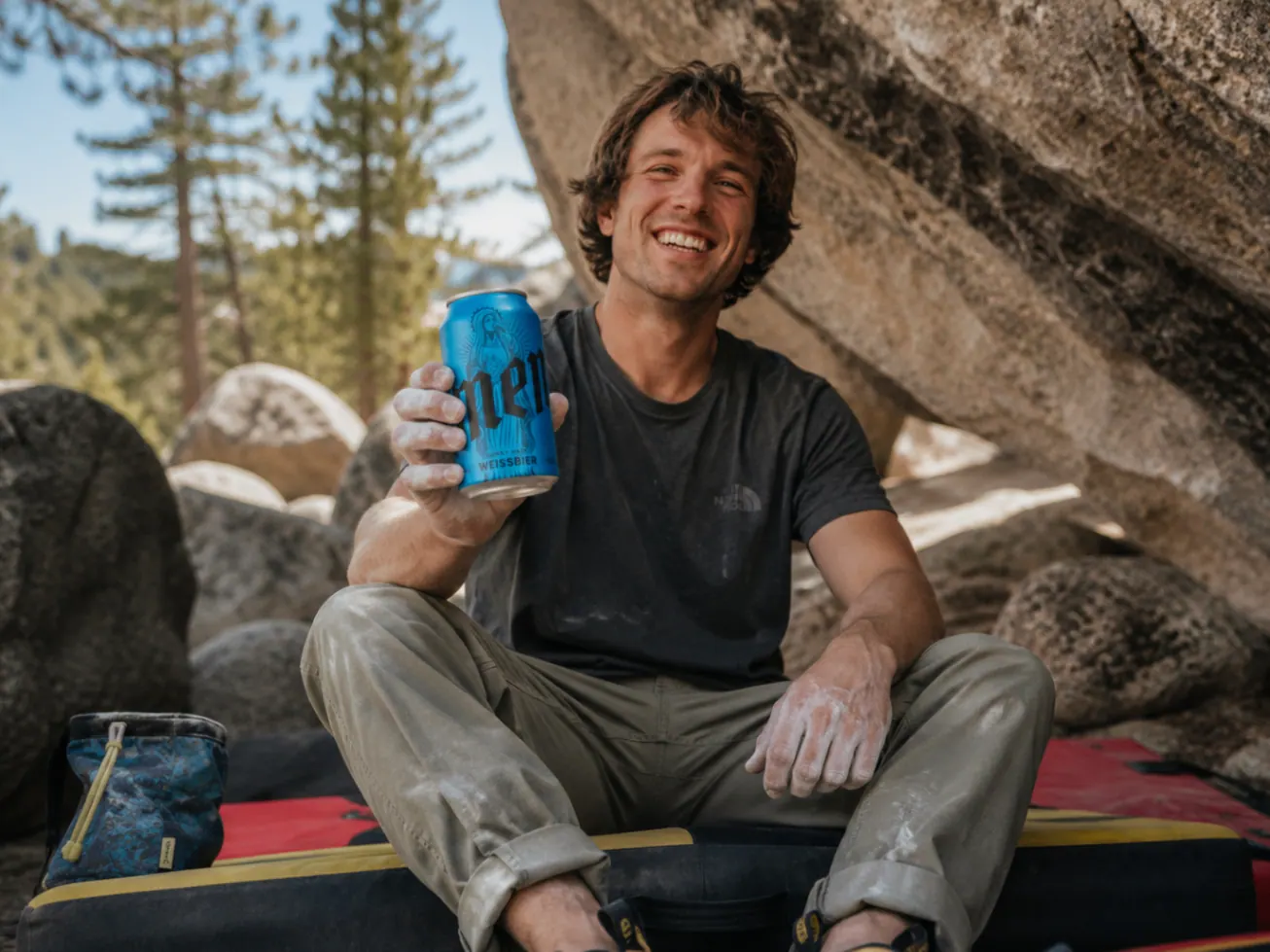 Climber smiling with a Weissbier can among boulders