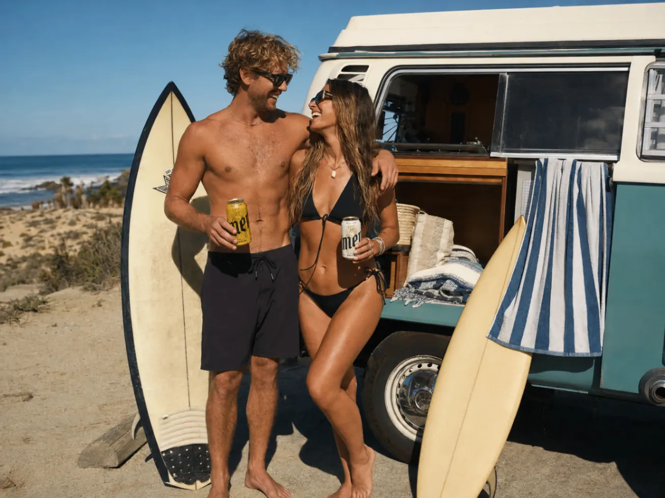 Beach couple by a surf van holding Amen cans